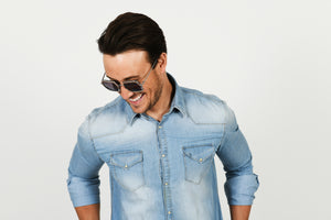 man wearing sunglasses and looking down and smiling wearing denim shirt